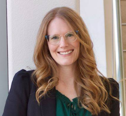 Alexis who has curly red hair, glasses, and is wearing a black blazer and a green blouse